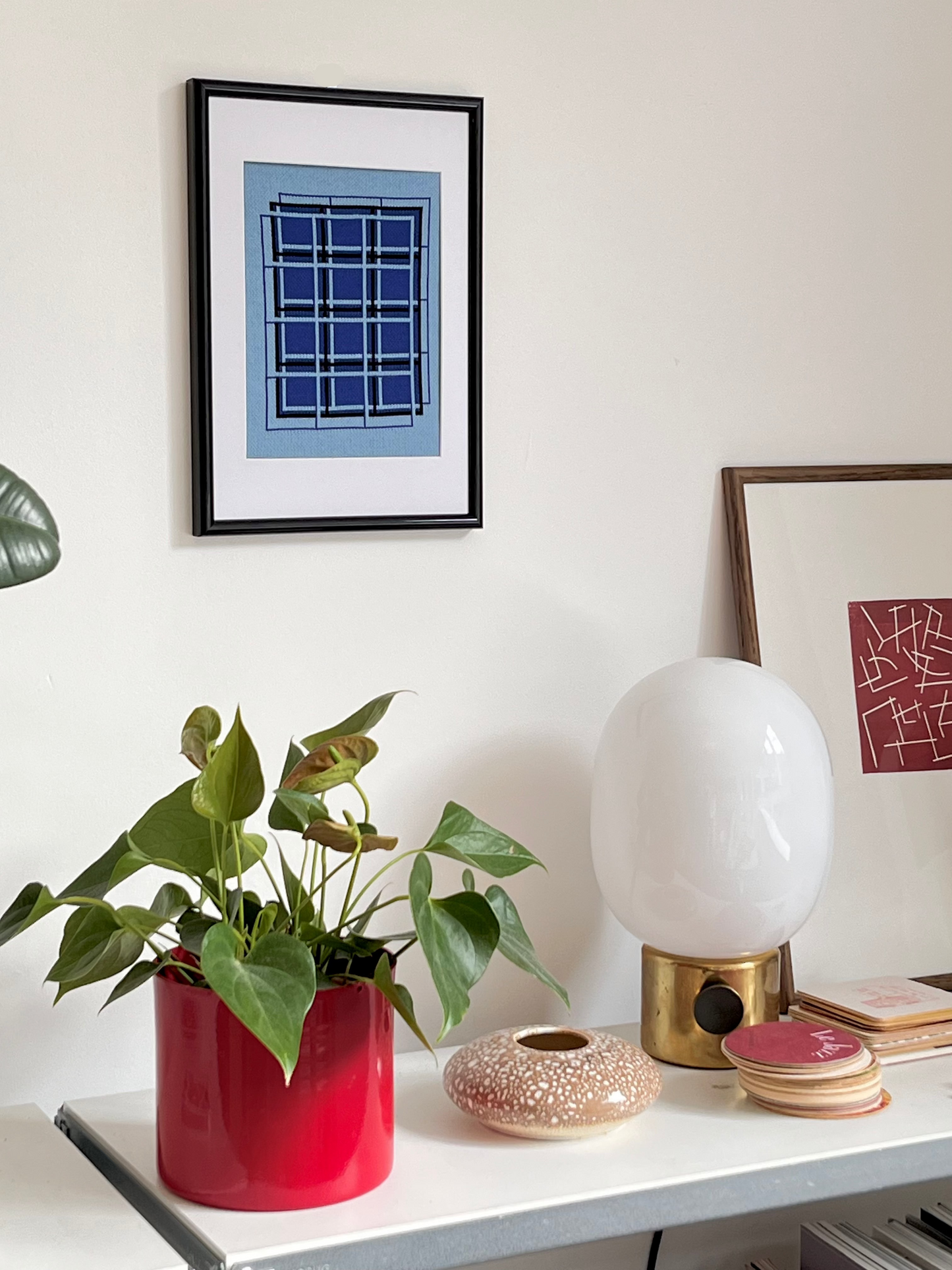 Decorative items on a shelf including a plant in a red pot, a white lamp, and framed artwork.