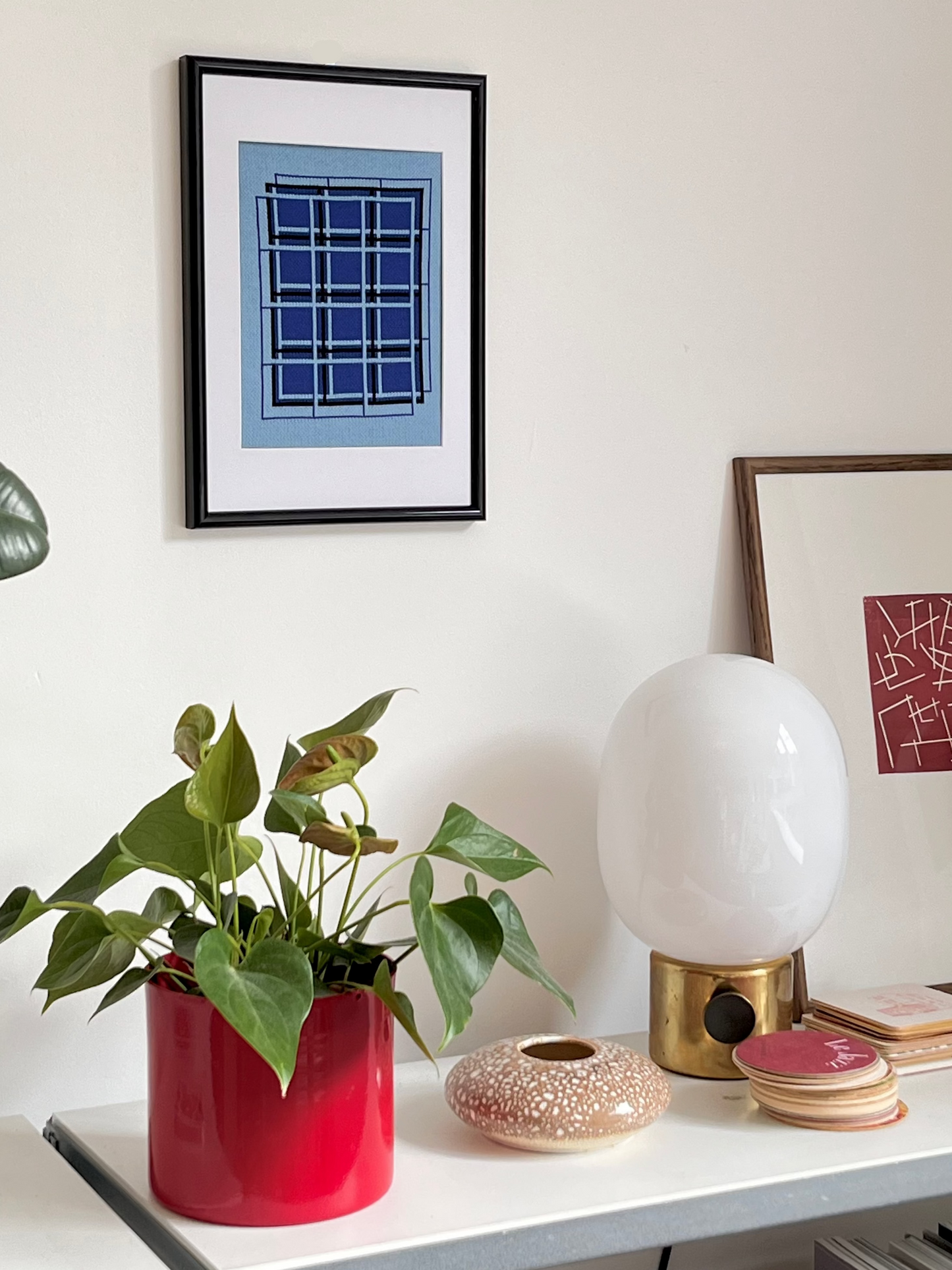 Decorative items on a shelf including a plant in a red pot, a white lamp, and framed artwork.