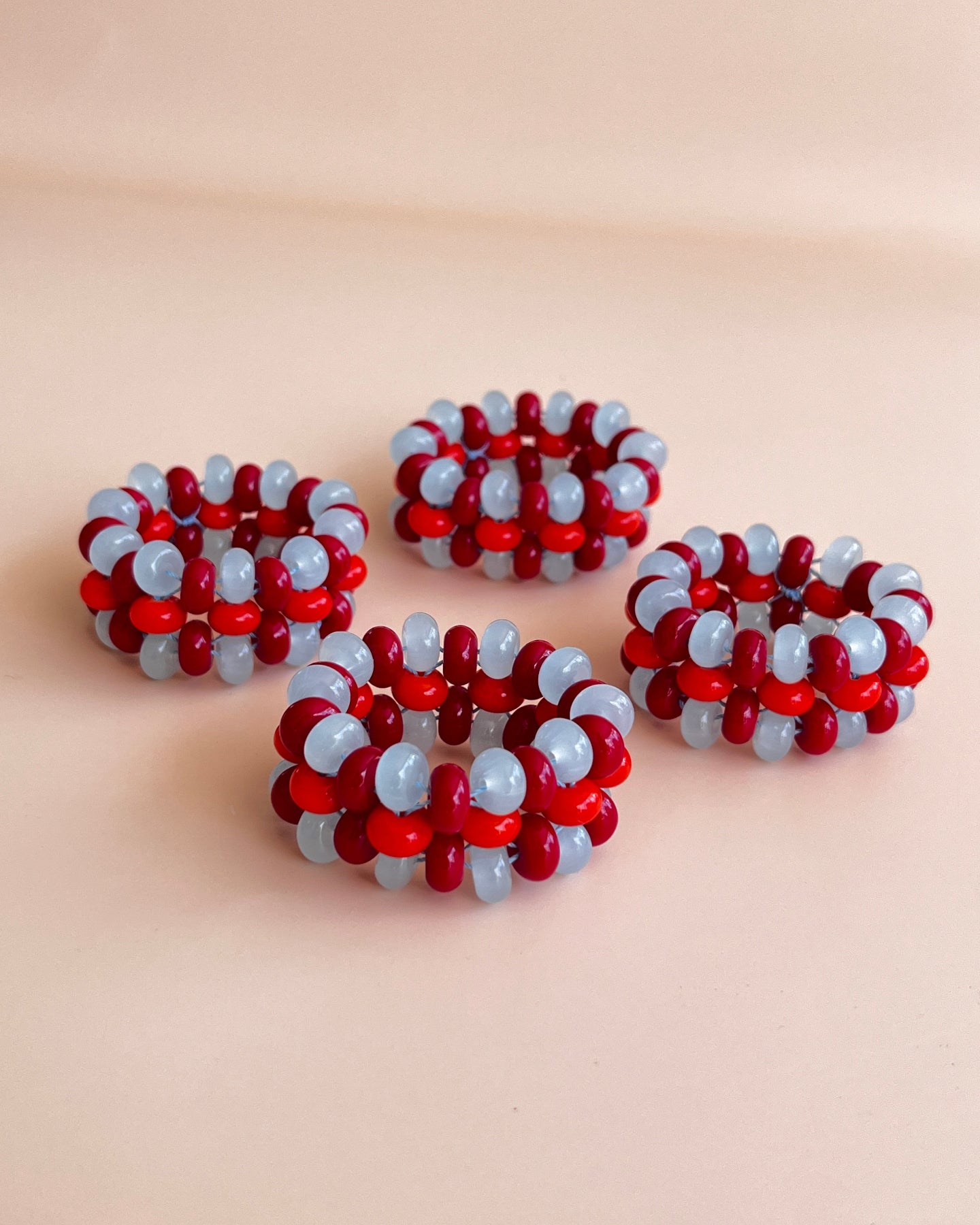 Four handmade beaded rings with alternating red and light blue beads, arranged on a soft beige background.