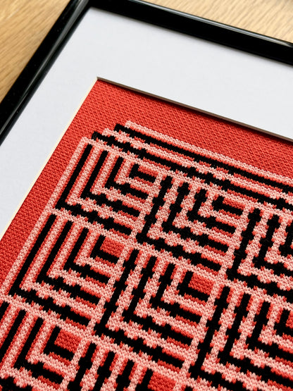 Framed textile with red and black geometric pattern on a wooden surface