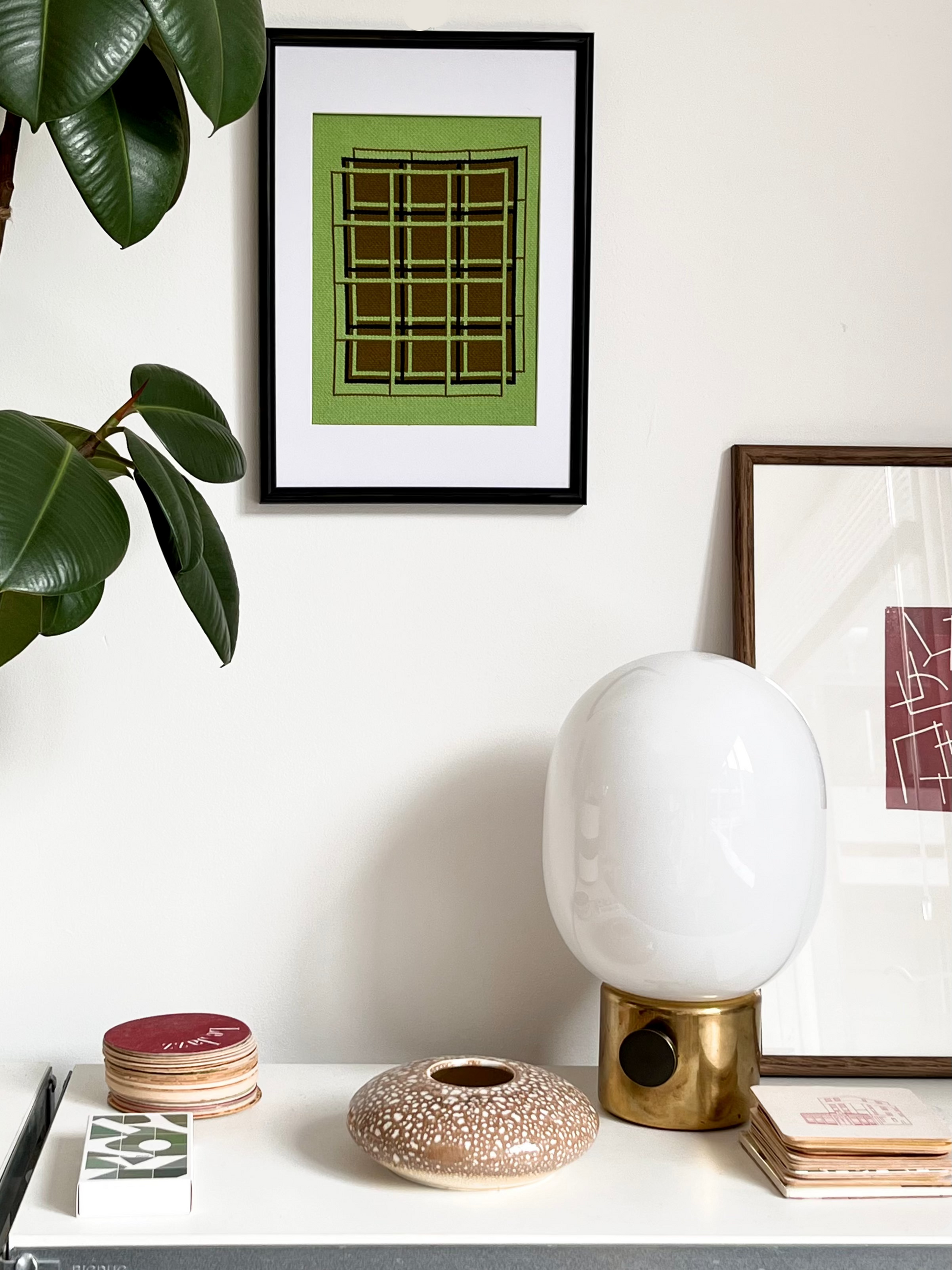 White lamp on a table with framed art and a plant in the background