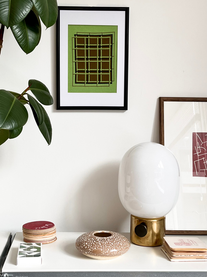 White lamp on a table with framed art and a plant in the background