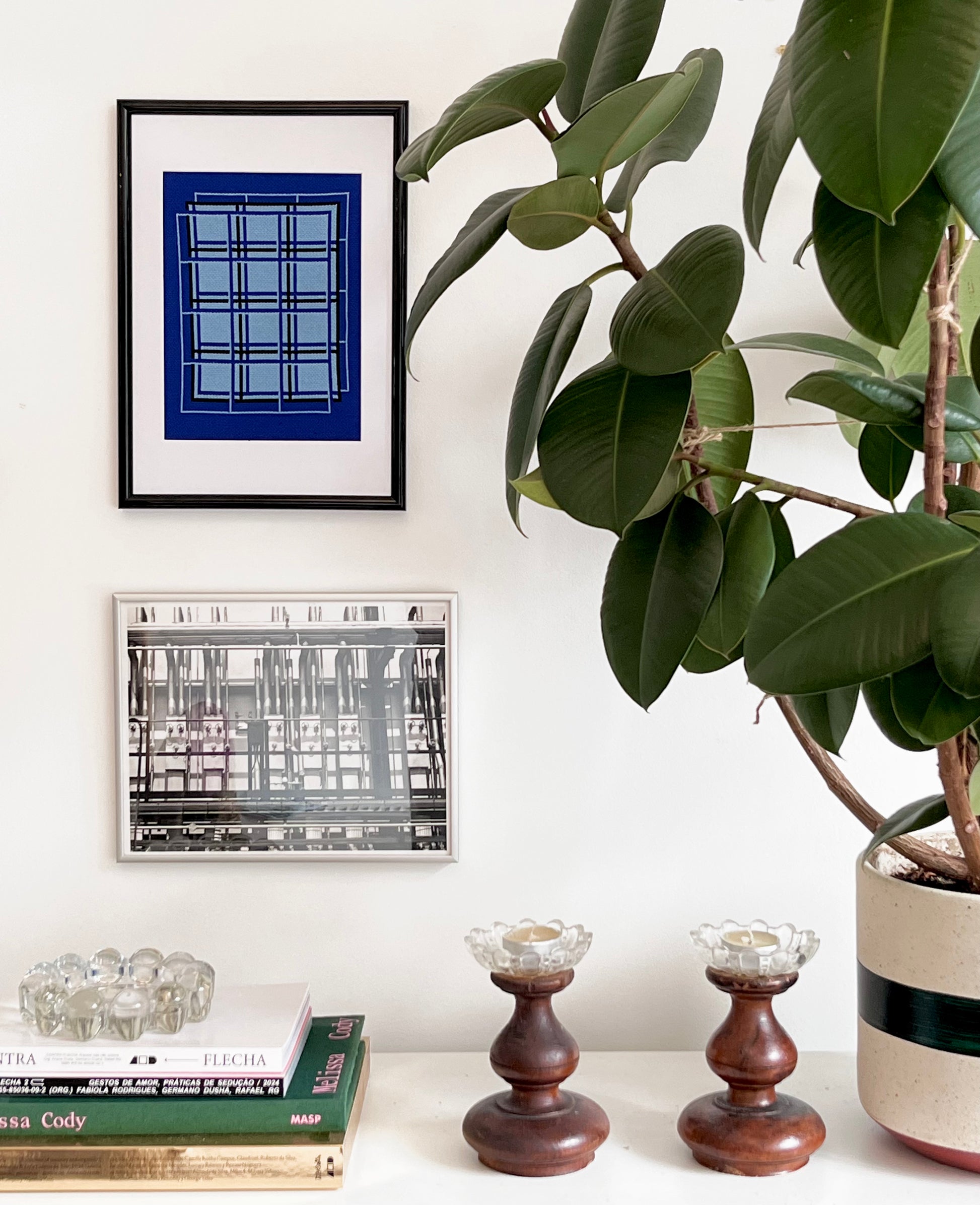 Decorative setup with framed art, books, candles, and a potted plant on a white surface.