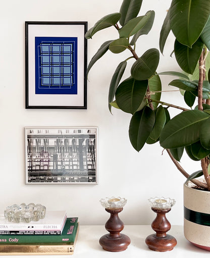 Decorative setup with framed art, books, candles, and a potted plant on a white surface.