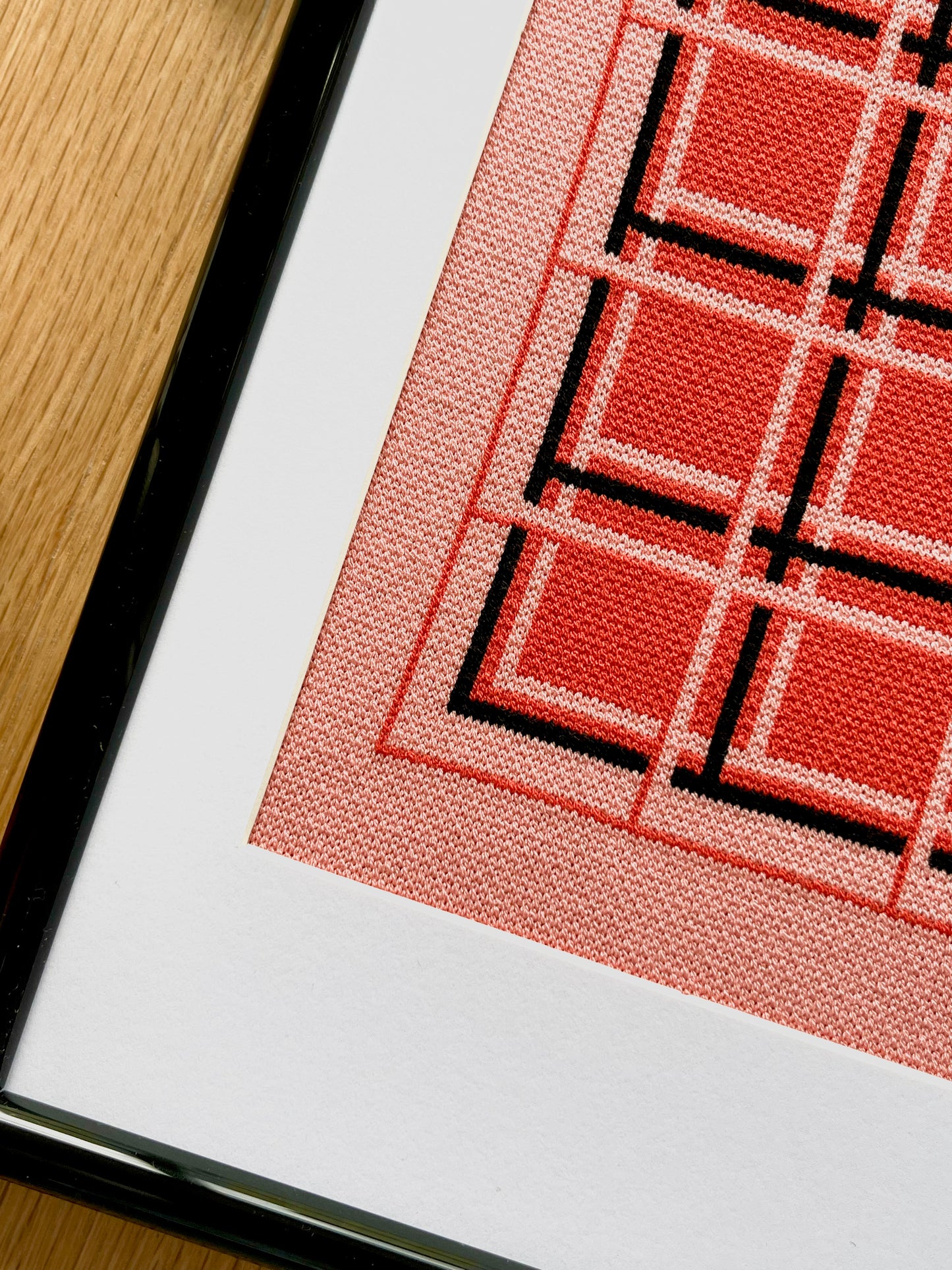 Close-up of a framed textile with red and black geometric pattern on a wooden surface