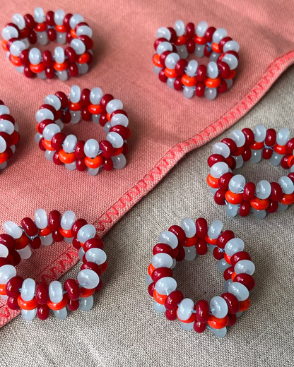 Several handmade beaded napkin ringsdarranged on a textured beige fabric with a pink stitched cloth underneath. Home decor glass beads retro. Ambar London UK