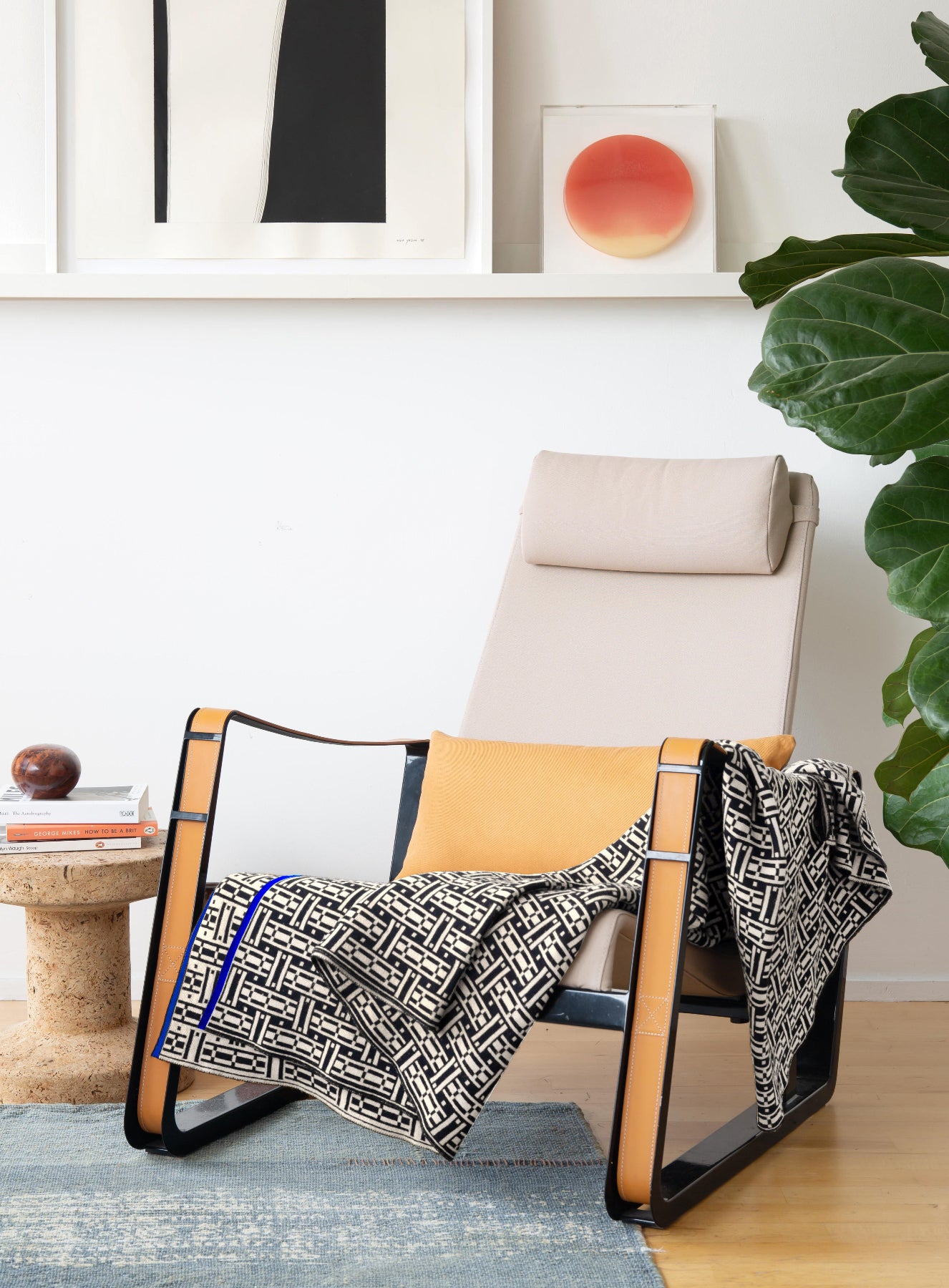 Modern chair with a patterned blanket in a room with framed artwork and a plant.