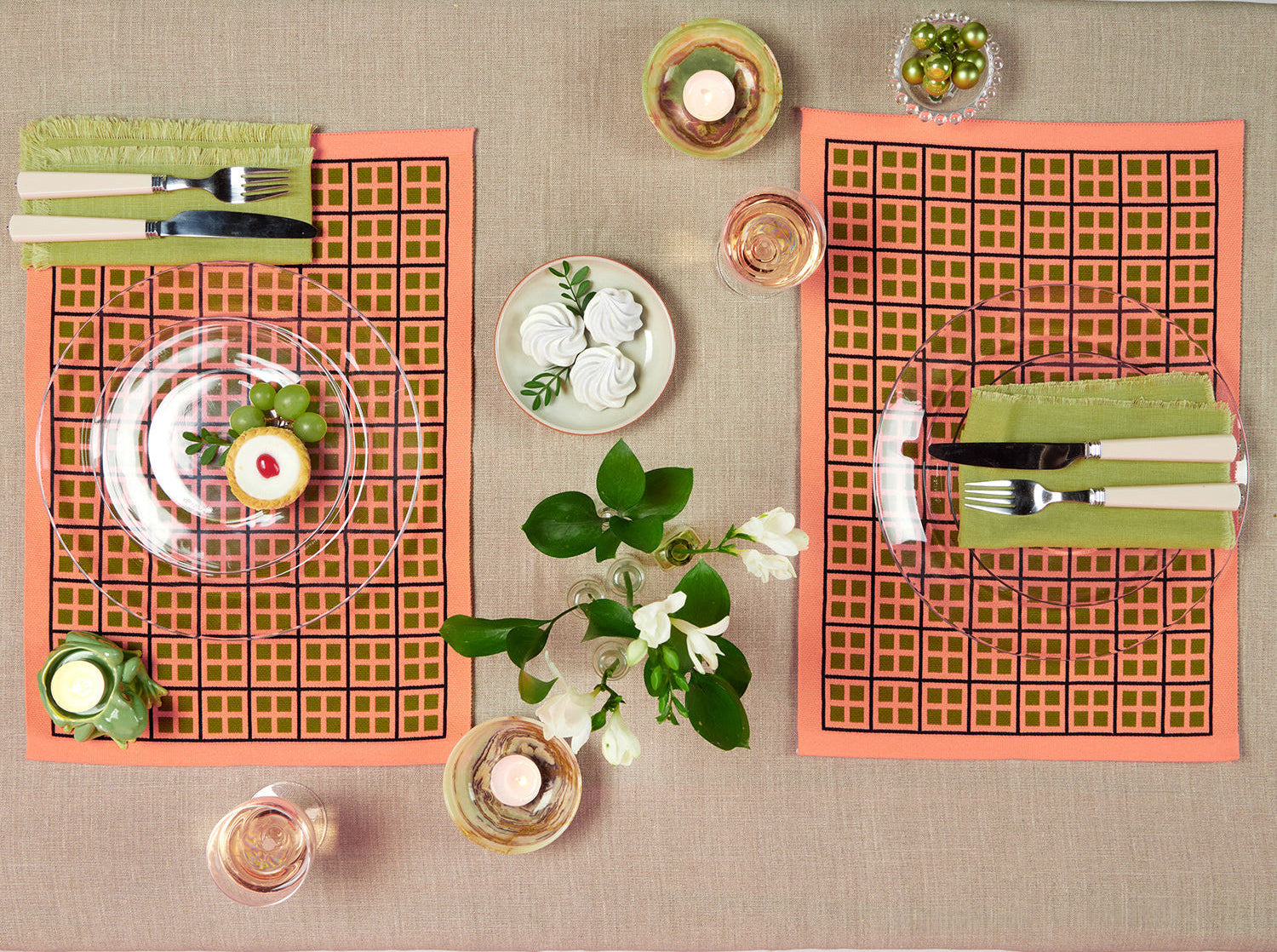 Table setting with pink checkered placemats, white plates, and green napkins on a beige tablecloth.