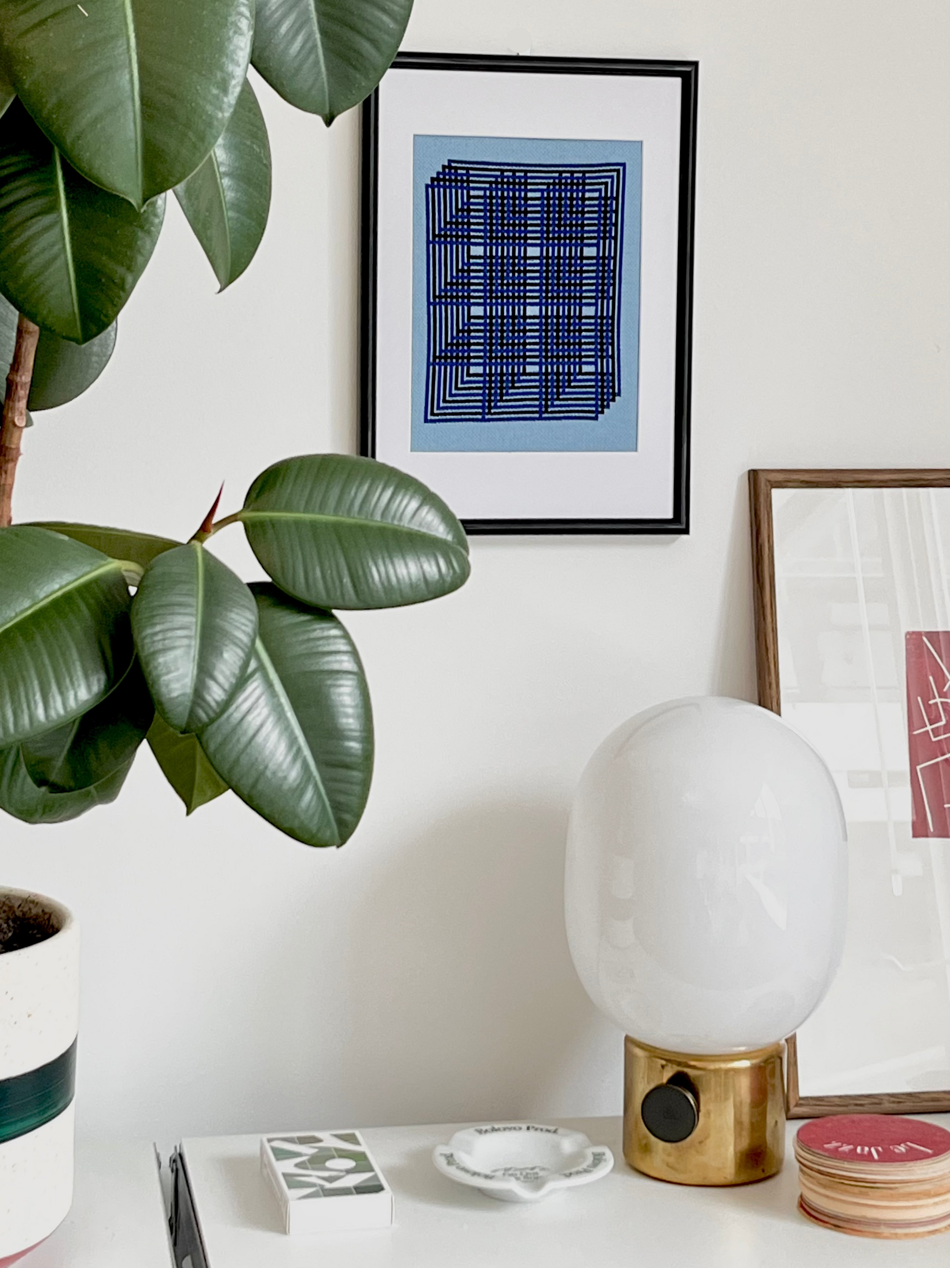 Decorative interior with a plant, lamp, and framed art on a white wall.