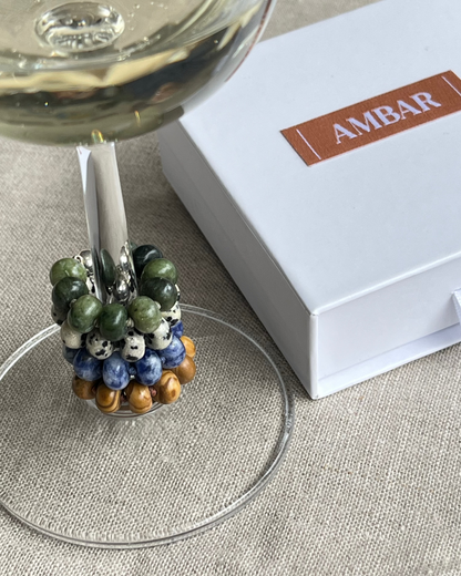 Decorative wine glass charm with colored beads on a glass, next to an 'AMBAR' branded box.