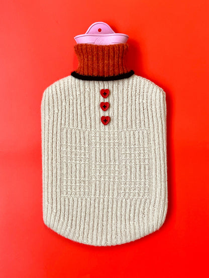 Hot water bottle with a beige knitted cover and red heart buttons on a red background