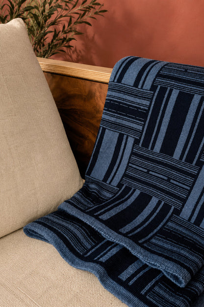 Blue patterned blanket draped over a beige sofa with a wooden armrest.