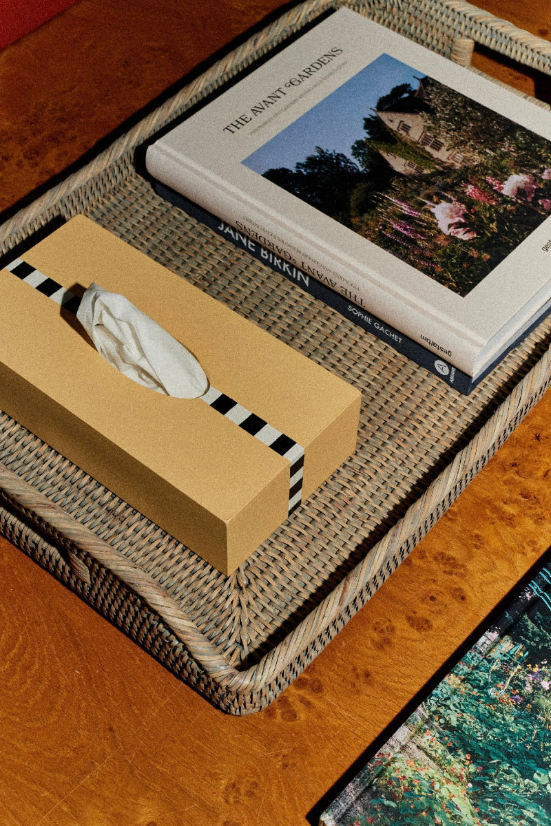 Book and tissue box on a woven tray with a blurred painting in the background